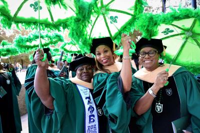 Robed students at graduation holding decorative Tulane umbrellas. 