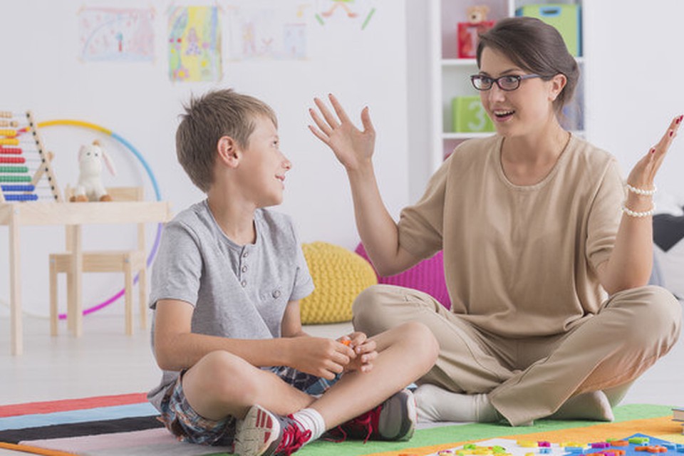 A boy seated at the floor looking at a woman, who is also seated on the floor and has her hands up while talk to the boy