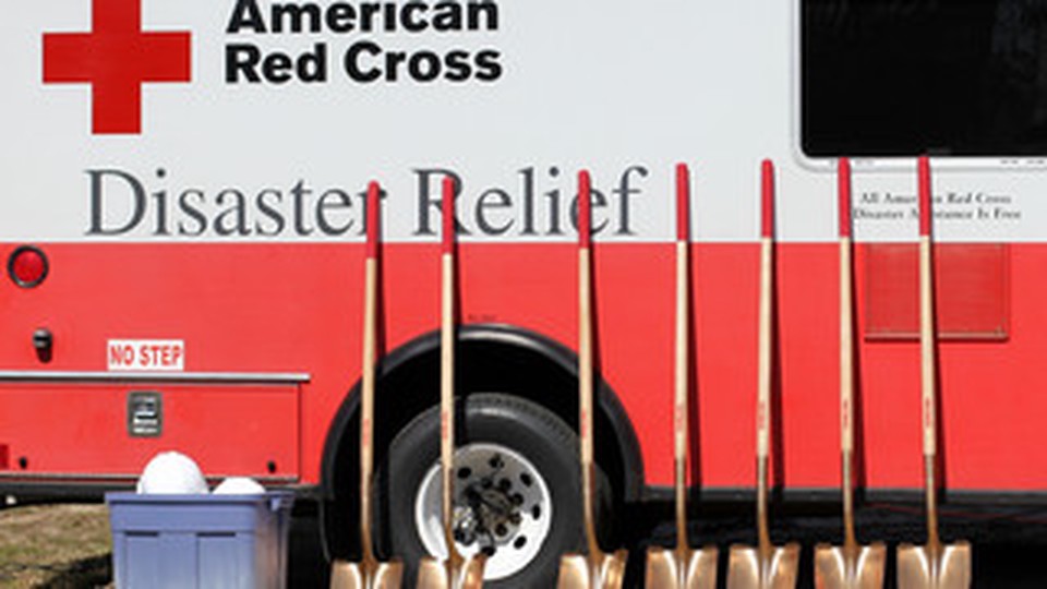 An ambulance from the American Red Cross - Disaster Relief parked with shovels leaning against it