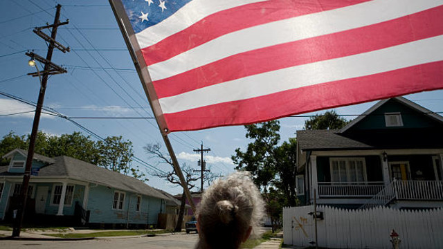 A woman stands on a neighborhood street facing the American flag