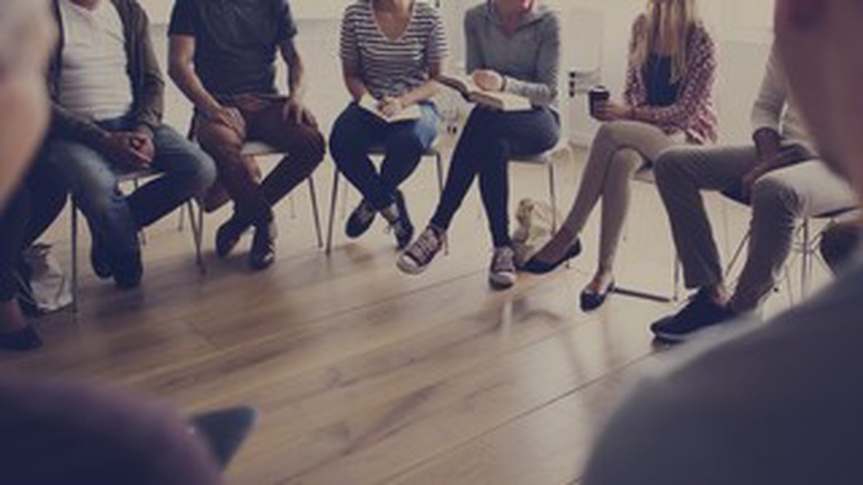 A circle of people seated on chairs but their faces are not shown.