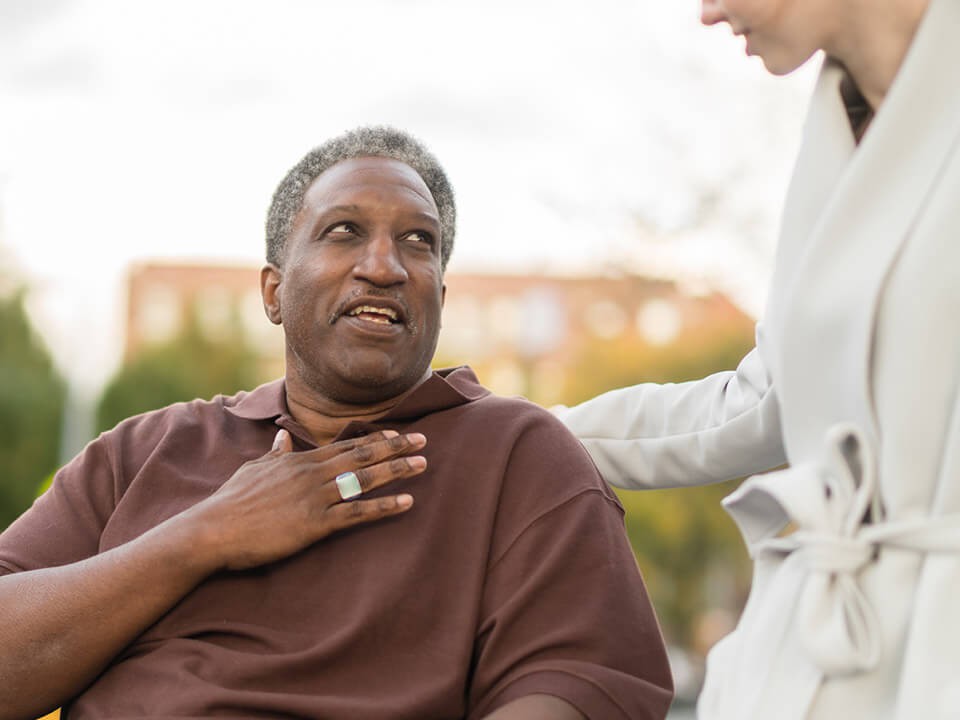 A man, seated, looking at a woman who is standing up. The woman's head is not visible