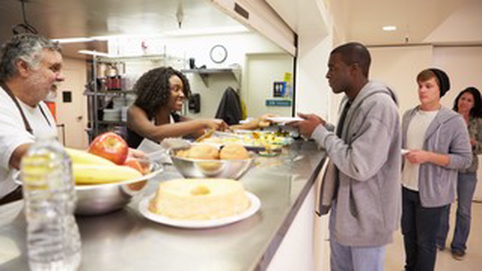 Two people serving food to a man, another man and woman are in line