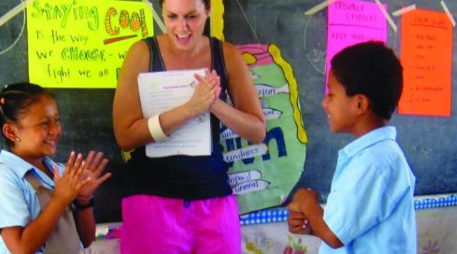 A teacher holding papers claps her hands along with two of her students