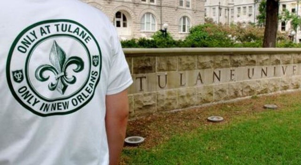 On the campus of Tulane University, a student wearing a Tulane t-shirt stands in front of campus buildings