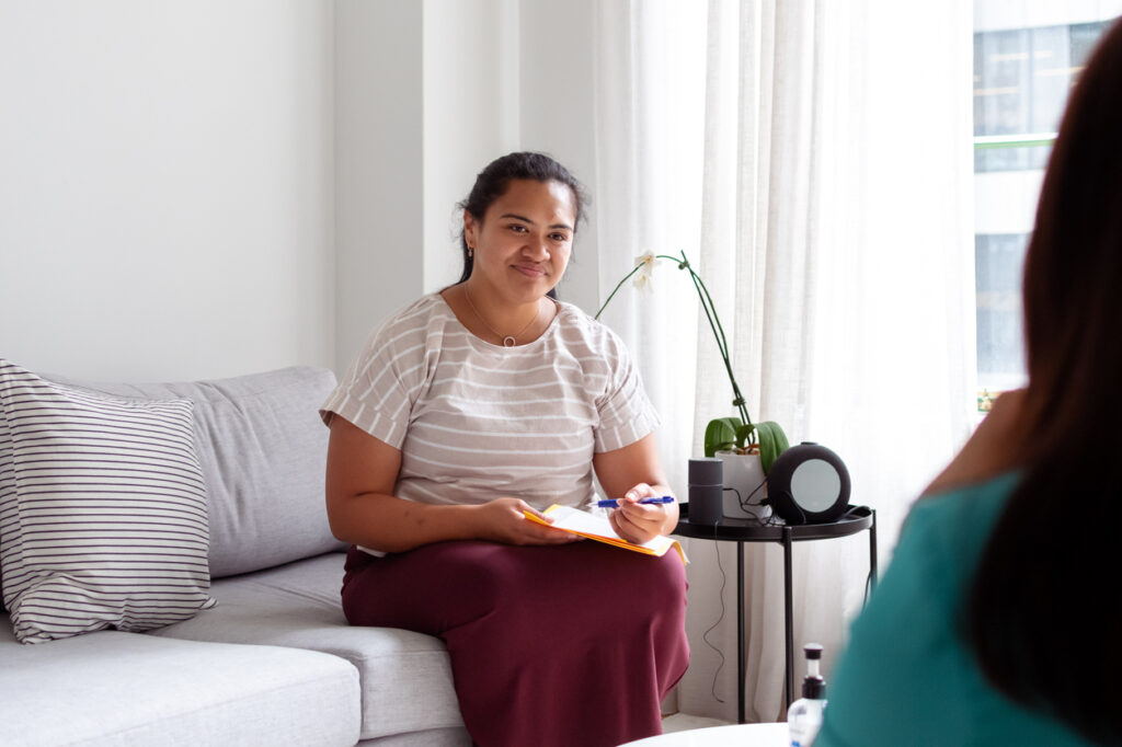 Social worker holding a clipboard and sitting with a client.