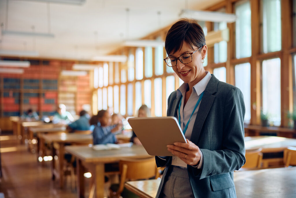 A professor standing in a classroom uses a tablet device.